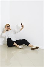 Funny woman sits on a floor in bright room and making selfie with smartphone
