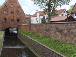 Canal flows under a brick bridge with neighbouring historic buildings and a stone wall, Gdansk,