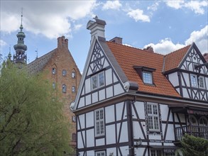 Traditional half-timbered house with a red tiled roof, next to a high brick tower, blue sky and