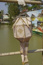 Traditional Chinese lantern with golden decorations, hanging from a bamboo pole over water,