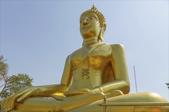 Large golden Buddha statue in lotus position in front of clear sky and trees, Pattaya, Thailand,