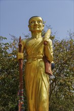 Golden monk statue in front of a natural setting of trees and blue sky, Pattaya, Thailand, Asia