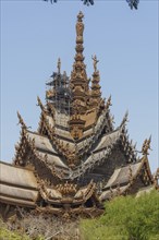 Detailed wooden temple with numerous sculptures and artistic elements against a blue sky, Pattaya,