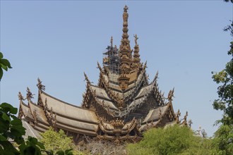 Wooden temple with ornate sculptures and detailed architecture against a clear sky, Pattaya,