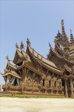Close-up of a wooden temple with rich sculptures and reliefs, blue sky in the background, Pattaya,