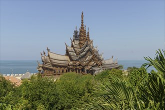 Wooden temple with intricate architecture surrounded by lush greenery, with the sea and blue sky in
