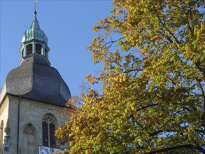 Church tower rises into a clear, sunny autumn sky, surrounded by colourful leaves, nottuln,