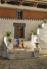 Two kids in colourful traditional clothes walking up the stairs inside Trongsa dzong