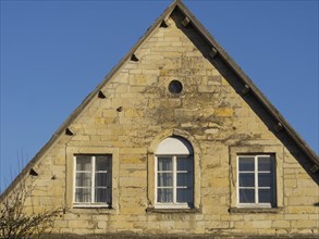 Front of an old brick house with two windows and a pointed roof gable under a blue sky, nottuln,