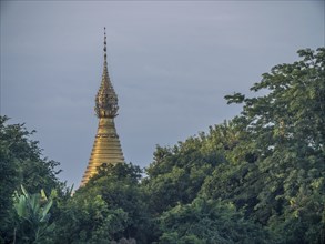 Golden stupa behind green trees at the Irrawaddy river