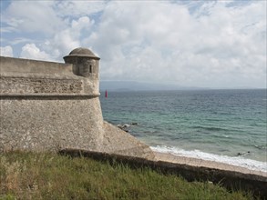 Historic coastal fortress with a view of the sparkling sea on a cloudy day, ajaccio, corsica,