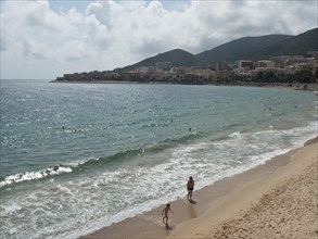 People walking along a sandy beach with a coastal town in the background, ajaccio, corsica, france