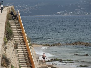 A man walks down to the beach via a coastal staircase overlooking the sea, ajaccio, corsica, france