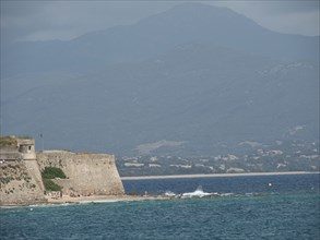 Ancient fortress wall on the coast with a view of the sea and cloudy mountains in the background,