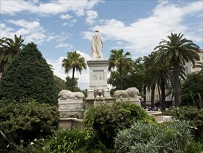 An impressive statue of a lion in a fountain surrounded by palm trees in a park under a cloudy sky,