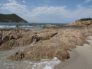 Rocky shoreline with smaller waves reaching the shore under a blue sky, ajaccio, corsica, france