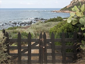 Black wooden gate leads to a coastal landscape with plants and sea views, ajaccio, corsica, france
