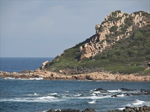 Rocky cliffs with plants and the sea with waves under a blue sky, ajaccio, corsica, france