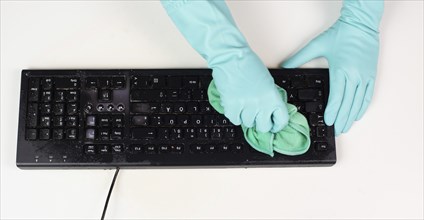 Cleaning computer keyboard in office with a wet wipe rag, dusty and dirty electronic, housework
