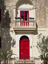 Charming building with bright red windows and doors and a small balcony with flowers, mdina,