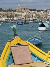 View from the bow of a boat of a harbour town with several boats in the water, marsaxlokk,