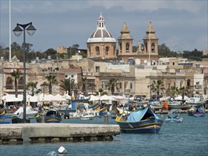 Fishing boats in the harbour with a cathedral in the background under a cloudy sky, marsaxlokk,