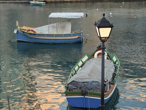 Two colourful fishing boats floating on a calm waterway with a lantern in the foreground,