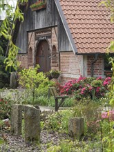 A garden with blooming flowers and stones, in front of a half-timbered house with a tiled roof,