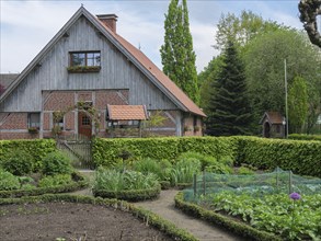 A half-timbered house with a large garden, including vegetable patches and surrounded by green