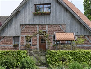 A half-timbered house with brick walls, a wooden gate and a green garden arch in front of the