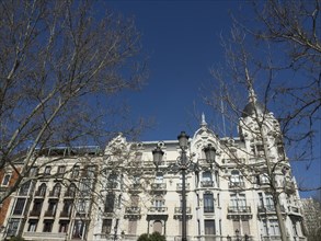 Large building with many windows and balconies, surrounded by bare trees and blue sky, Madrid,