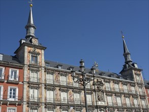Large historic building with towers and clock, surrounded by lanterns under a blue sky, Madrid,