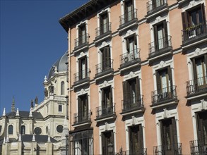 Historic buildings with many windows and a church in the background under a blue sky, Madrid,