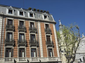 Multi-storey building with many windows, next to a historic building and trees under a clear sky,