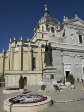 Statue in front of a church with flower beds in a sunny square under a clear sky, Madrid, Spain,