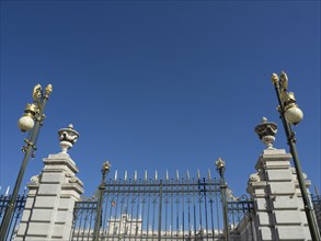 Black, wrought-iron fence with golden decorations encloses a historic building under a clear sky,