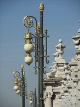 Ornamental lanterns with golden accents in front of a decorative white historic building under a