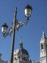 Decorative street lantern in front of historic buildings and towers with a dome under a blue sky,