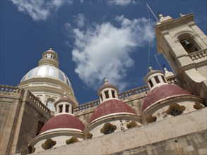 Cathedral with a large white and three red domes, as well as a bell tower, under a cloudy sky,
