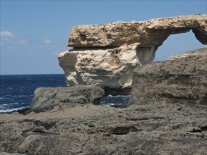 Structure formed by a rocky arch on the coast with wild sea and a rocky rugged landscape, gozo,