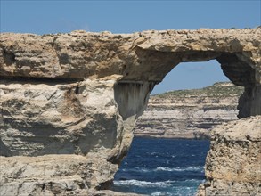 Naturally formed rock arch on the coast with the blue sea in the background and a rocky landscape,