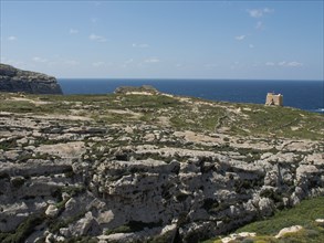 Rocky coastline with an old watchtower and sweeping views of the blue sea and sky, gozo,