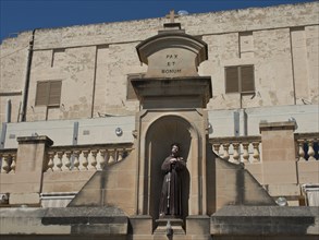 Statue of a monk in a stone niche in front of a historic building, stone wall with inscription Pax