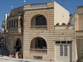 Two-storey sandstone building with balconies and flowers on a sunny day, Gozo, Mediterranean,