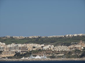 Mediterranean coastal town with a view of several buildings on a hill under a blue sky, gozo,