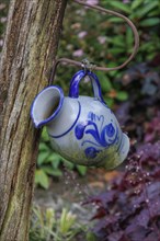 Close-up of a blue and white decorative jug hanging from a wooden post in a flowery garden, Borken,