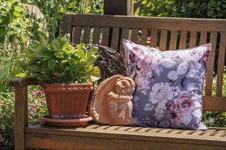 A decorative arrangement on a wooden bench with a floral patterned cushion, a terracotta pot and a