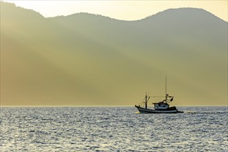 Fishing trawler sailing in front of the mountains of Ilhabela during sunset, Ilhabela, Sao Paulo,