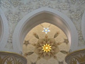Ornate ceiling with intricate patterns and symmetrical design illuminated by beams of light, abu