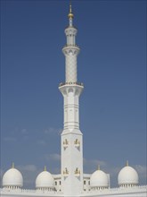 Tall minaret with elaborate details, flanked by domes under a blue sky, abu dhabi, united arab